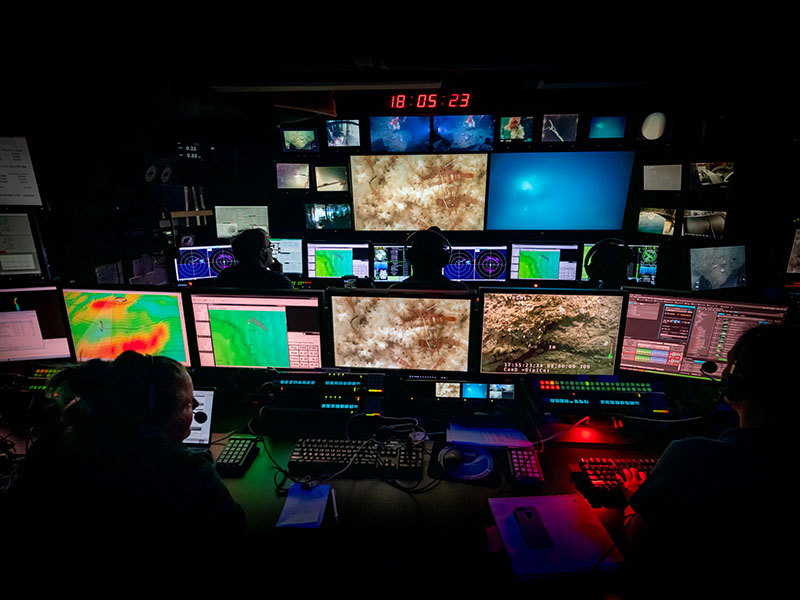 During remotely operated vehicle (ROV) operations, ROVs Deep Discoverer and Seirios are controlled by navigators and pilots, and the exploration is led and narrated by scientists in the mission control room of NOAA Ship Okeanos Explorer, seen here, who watch the video feeds from the ROVs in real time. The same feed is transmitted to shore via telepresence.