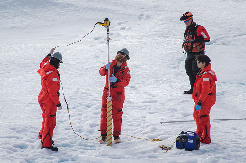 The science team handles the ice corer to collect ice samples.