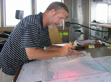 First Mate Mike Schoeller checks his charts to confirm the ship's faster-than-expected transit time to its first dive location. First Mate Mike Schoeller checks his charts to confirm the ship's faster-than-expected transit time to its first dive location.