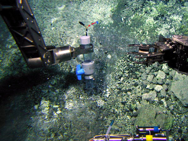 The manipulator arm of Pisces V holds a gas-sampling device over a vent where bubbles are streaming out.