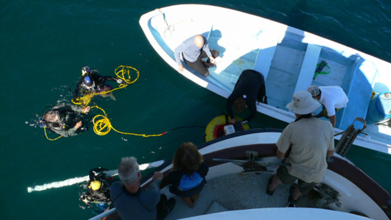 The crew on the ship watch as the divers prepare to submerged with the airlift device.