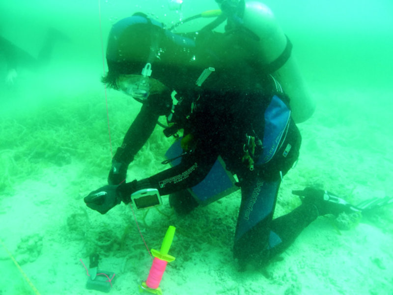 Kaya Chotard ties string to a weight on one end and a plastic bottle on the other end. The weight will mark a place on the sea floor while the plastic bottle will float to the surface and act as a marker for an area that will be tested on a subsequent dive.