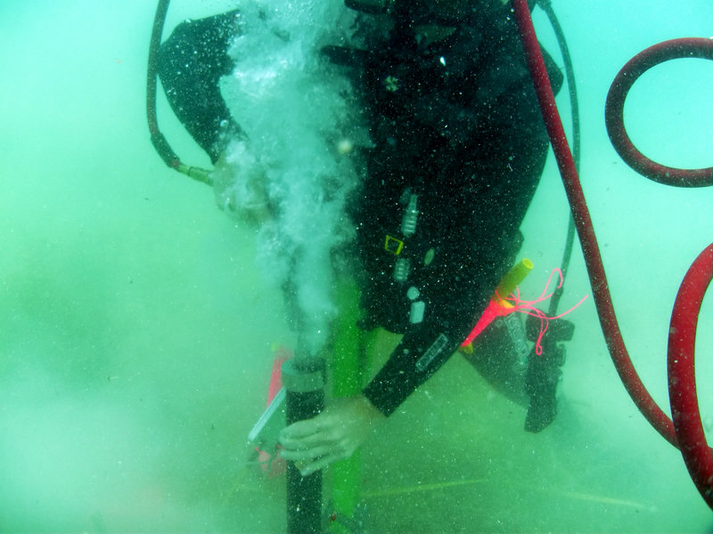 Diver operating the pneumatic corer. The airgun has a specialized head that holds a PVC pipe. The device is attached to a surface supplied airsource.