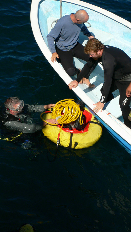 Clint Nelson hands Loren Davis the motor and the airhose for the airlift device. The motor is attached to an air compressor that floats on the surface and pushes air down the hose into a PVC pipe that will suction material off the sea floor.