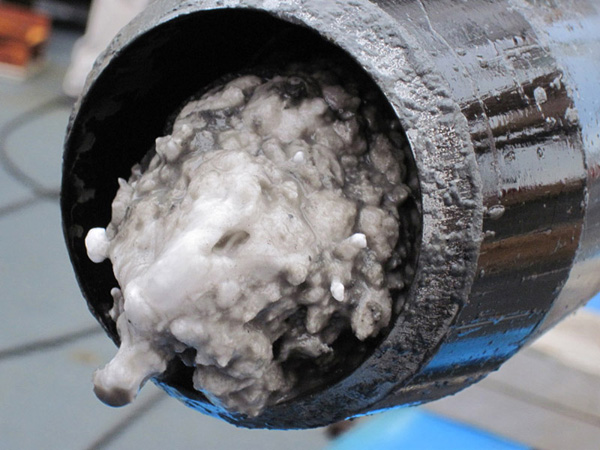 The piston corer, which hit bottom at about 2,550-m water depth, came back with gas hydrate in the core cutter at the bottom of the core barrel. Gas hydrate looks like water ice but is actually made up of water cages that enclose gas molecules, usually methane. Gas hydrate is stable at relatively low temperatures and moderate pressures like those beneath the seafloor at the coring site. At the surface, gas hydrate is not stable and breaks down (dissociates) into water and gas. Gas hydrate is sometimes called the 'ice that burns' because it will sustain a flame as the gas molecules are released.