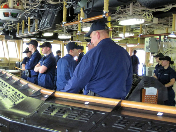 Conning officer Nick Custer (in doorway, monitoring the ship’s position as it moves away from the dock in Dutch Harbor) calls commands to helmsman Dierdre Gray (far right), who repeats and executes each command. Only two or three watchstanders are required when the ship is underway, but the bridge is busy with additional personnel during arrivals and departures.