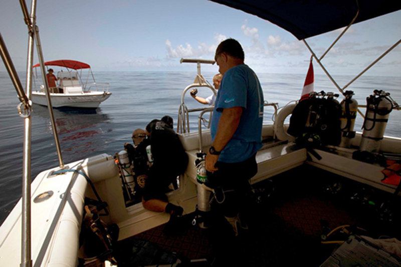 Brett Gonzalez assists Tom Iliffe with his bailout tanks as he prepares to dive on a beautiful flat sea.