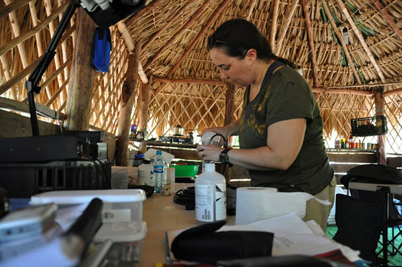 At the site’s main palapa, which served the expedition team as a work-space, kitchen, dining area and sleeping area, Trish Beddows calibrates the hydrolab in preparation of surveying the water chemistry of the site.