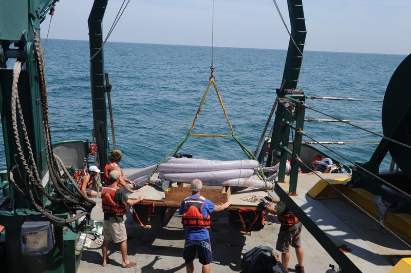 Crewmembers use the ship's A-frame to hoist the dredge and floating collection screen into the water.