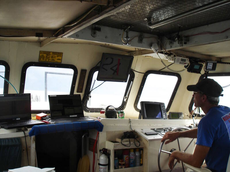 Inside the cabin of the Roper, Sam Turner mans the helm surrounded by computer displays. The two laptops on the left are the displays for the magnetometer and sidescan sonar respectively, while the monitor above Sam’s head shows the real-time position of the boat superimposed over the planned survey lane. During survey it is critical to steer the boat as truly as possible on the planned trackline, which can be a difficult task.