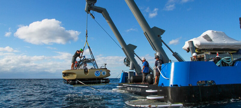 The manned submersible is being lifted out of water after its dive.