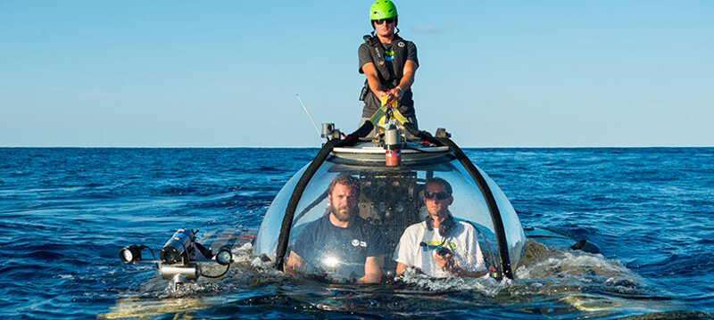 Randy Holt piloting the Triton submersible (right) with archaeologist John Bright onboard, and a technician helping the submersible return to the ship after the dive.