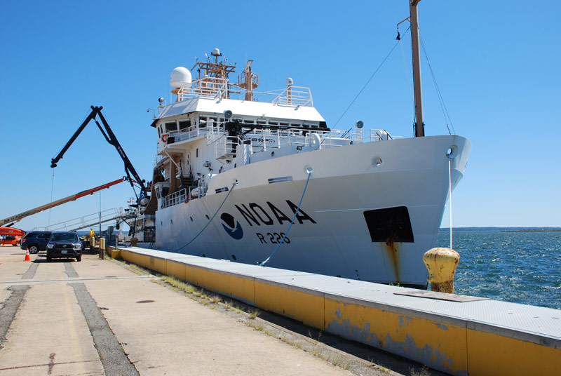 NOAA Ship Pisces sits dockside at NOAA Terminal 1 in North Kingstown, Rhode Island. Cranes in the background (one ship-based, one shore-based) serve to lift equipment to and from the ship.