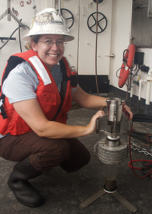 Amanda holds a monocore, an instrument used to collect a discrete sample of the bottom sediments.
