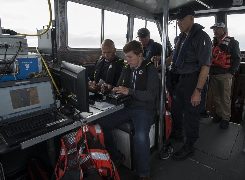 Hans VanSumeren (left, front) and John Lutchko (right, front) of Northwest Michigan College work together while piloting an ROV during investigations of newly discovered shipwreck sites in Thunder Bay National Marine Sanctuary during August, 2017. Members of the Michigan State Police Marine Services Team, who also participated in the investigations, observe the operations onboard NOAA vessel R-5002.