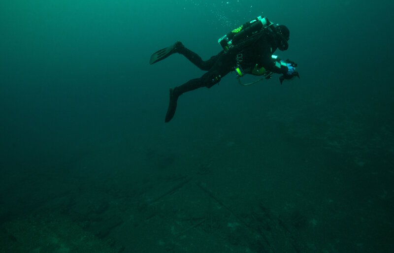 Phase IV started with a series of ‘work-up’ dives used to practice technical diving techniques and refine the photogrammetric imagery acquisition protocols before visiting deeper sites. Here, NOAA Diver Joe Hoyt swims above the debris field off the stern of wooden bulk carrier New Orleans. He maintains a consistent altitude off the bottom, necessary to ensure broader coverage of the debris field features as the relate to the main vessel remains. Source: NOAA, Thunder Bay National Marine Sanctuary.