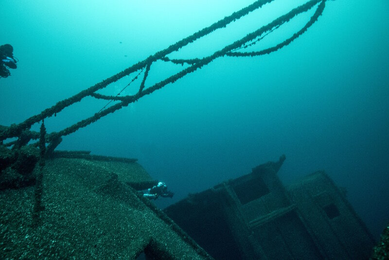 The three-diver bottom team dynamic is demonstrated here where NOAA Divers John Bright (center of image) and Joe Hoyt (taking the photograph) move in tandem down the length of bulk carrier Norman capturing imagery while the in-water safety diver—Eastern Carolina University Reciprocity Diver Mark Keusenkothen (top left)—hovers above and in between each diver.