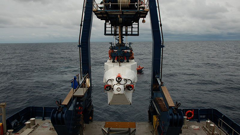 Swimmers Todd Litke and Drew Bewley sit atop Alvin as its lowered from the A-frame into the water. Once in the water, the swimmers are responsible for disconnecting the lines and communicating with the pilot inside to ensure that the sub is ready for descent.