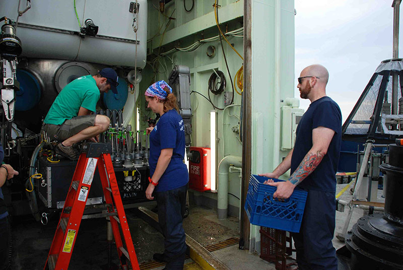 Erik Cordes unloads the Alvin sample basket as Jennie McClain-Counts and Jonathan Quigley standby ready to haul a crate of pushcores back to the cold room.