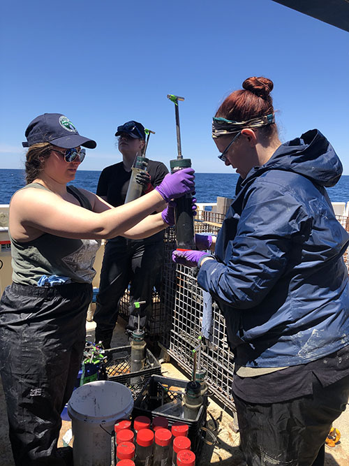 Allyson Boggess holds a push core collected from Pamlico Canyon while Jill Bourque places a rubber stopper in the bottom for safe storage before processing begins.