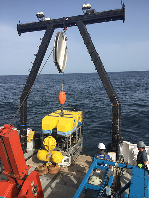 The crane lifts the ROV and its experimental cargo into the ocean.