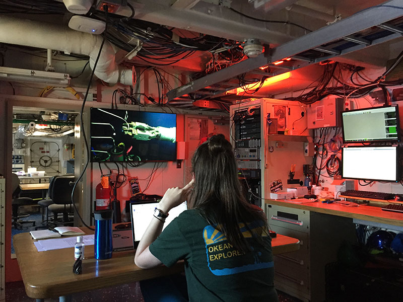 NOAA Ocean Exploration representative Anna Lienesch in NOAA Ship Nancy Foster dry lab watching the remotely operated vehicle control pull a Niskin bottle for water sample from a midwater trisect during the Illuminating Biodiversity in Deep Waters of Puerto Rico 2022 expedition.