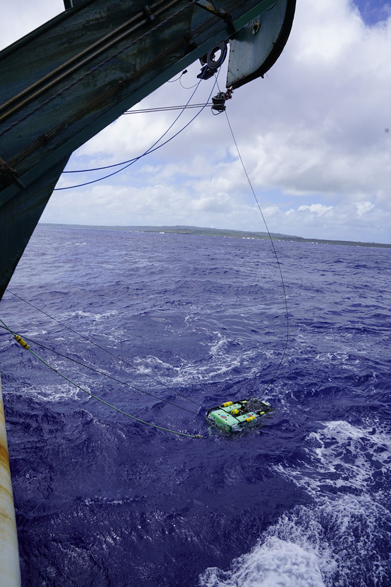 The ROV has been lowered into the water, and the green umbilical cable is visible. During the expedition, the ROV will be used to collect imagery at locations with anomalies identified in the side-scan sonar data collected by the REMUS 600 vehicles during the Deepwater Surveys of World War II U.S. Cultural Assets in the Saipan Channel expedition.