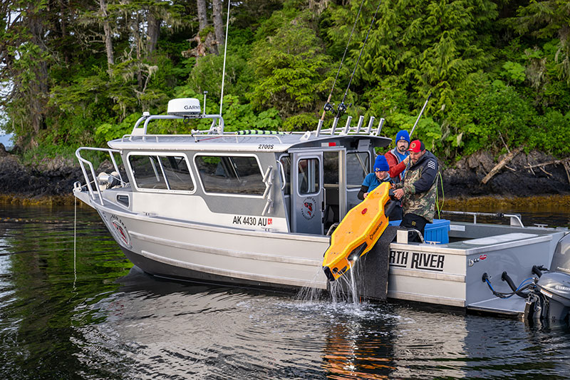 Robotics technician Mimi Alexander, left, and captain Roby Medina haul autonomous underwater vehicle SUNFISH back onto the boat after a 2023 Our Submerged Past survey mission while project co-investigator Kristof Richmond, center, minds the fiber optic cable connecting SUNFISH to mission control on the boat.