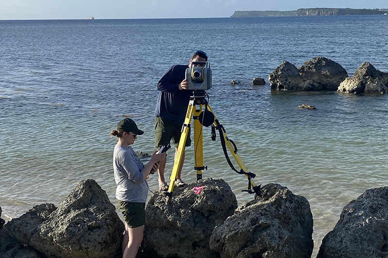 Anne Wright and Tahzay Jones preparing a Trimble SX10 scanning total station to collect high-density, high-accuracy elevation data along the coastline in the Agat unit of War in the Pacific National Historical Park.
