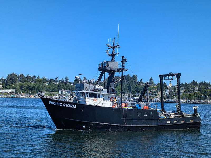 Research vessel 'Pacific Storm' on the water with shoreline in the background.