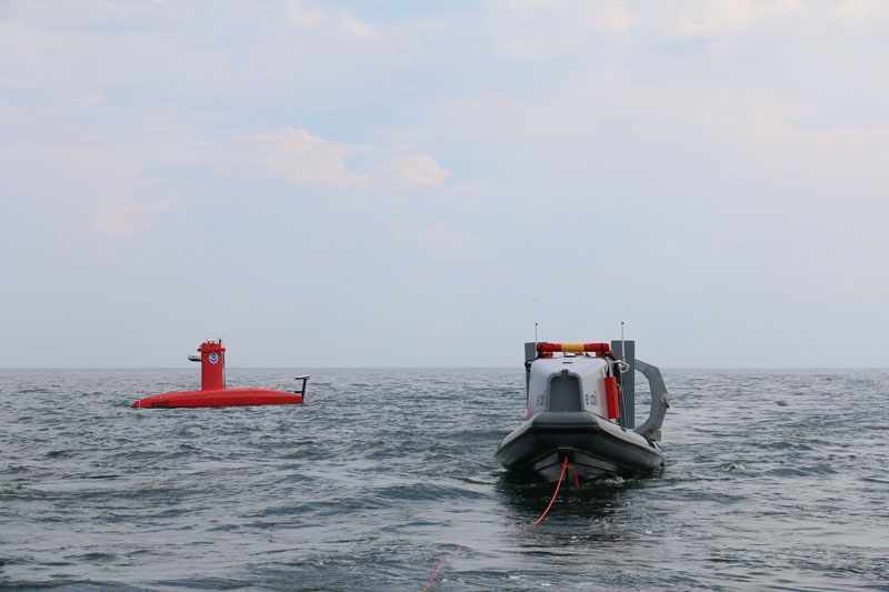 A DriX uncrewed surface vehicle surveys in the distance behind its deployment system.