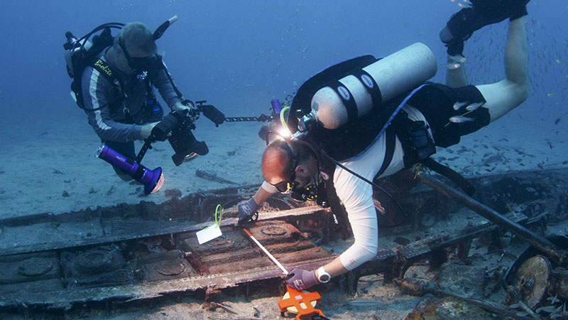 Archaeologists use measuring tapes and underwater cameras to record and document a World War II aircraft site in Papua New Guinea.