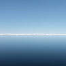 A stunningly blue and calm Arctic reflection of sea and sky divided by distant bright white ice and interrupted by ripples created by the ship. 15th June 2012 on the RRS James Clark Ross in the Arctic sea ice between Svalbard and Greenland.