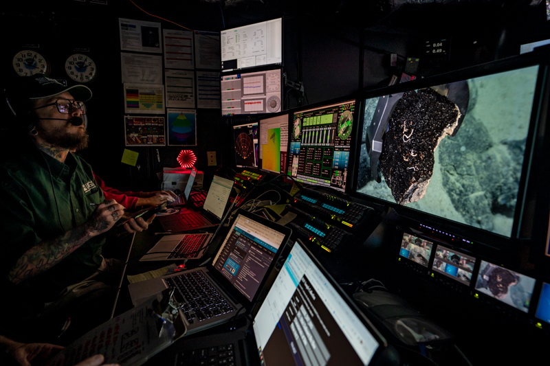 Voyage to the Ridge Expedition 2 geology science lead Ashton Flinders watches from the control room of NOAA Ship Okeanos Explorer as a rock sample is collected during Dive 07 of the second Voyage to the Ridge 2022 expedition.