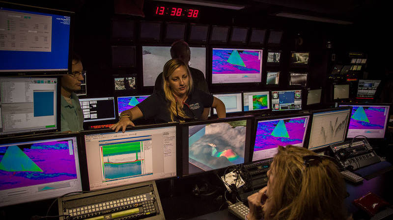 Meme explains to a group of members of the public touring the ship how Okeanos Explorer sonar systems acquire data and describes some of discoveries made using the sonar systems, including hundreds of gas seeps along the eastern seaboard.