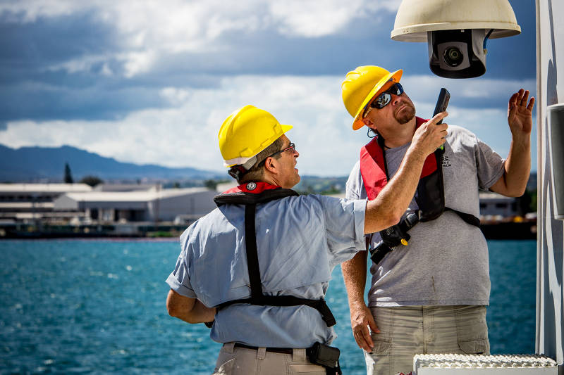 Video engineers Roland Brian and Joe Biscotti work on one of the robotic HD camera’s on the ship’s aft deck while the ship is in port in Pearl Harbor, Oahu.