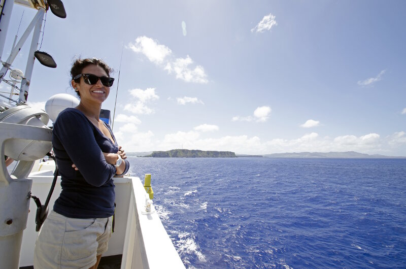 Leg 1 Biology Science Team Lead, Dr. Diva Amon, enjoying the view as NOAA Ship Okeanos Explorer heads to sea to start Leg 1 of the 2016 Deepwater Exploration of the Marianas Expedition. You can see the island of Guam in the background.