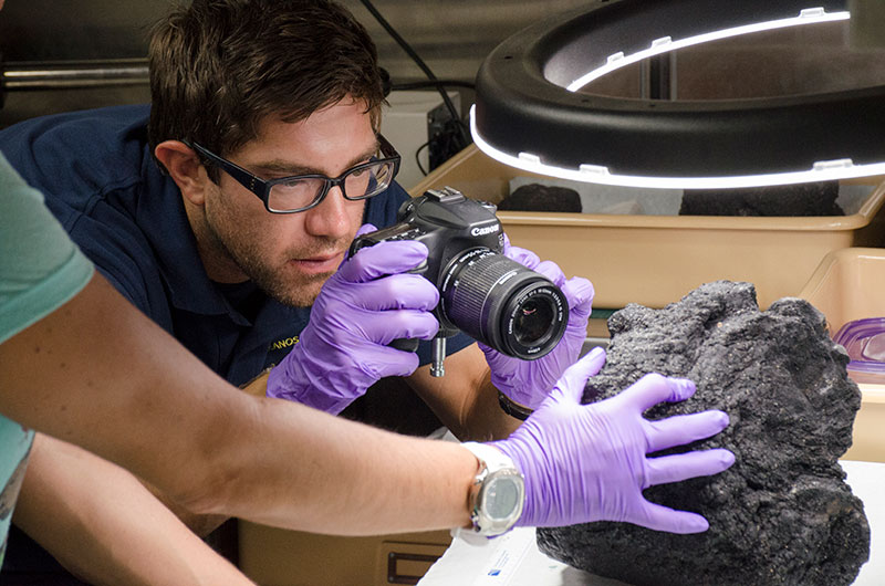 Matt Dornback, from the NOAA National Centers for Environmental Information, photographs a rock sample from the day’s dive. Rock samples are being collected during most dives for later age-dating and geochemical analysis to provide more information about the geologic history and age of seamounts in the Johnston Atoll Unit.