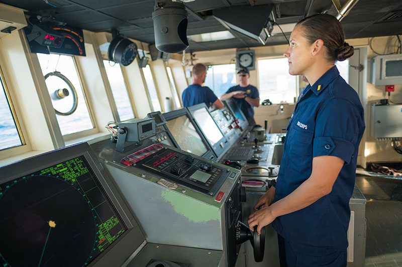 ENS Brianna Pacheco, one of the ship’s navigators, takes the helm and manually steers the ship on the bridge of NOAA Ship Okeanos Explorer.