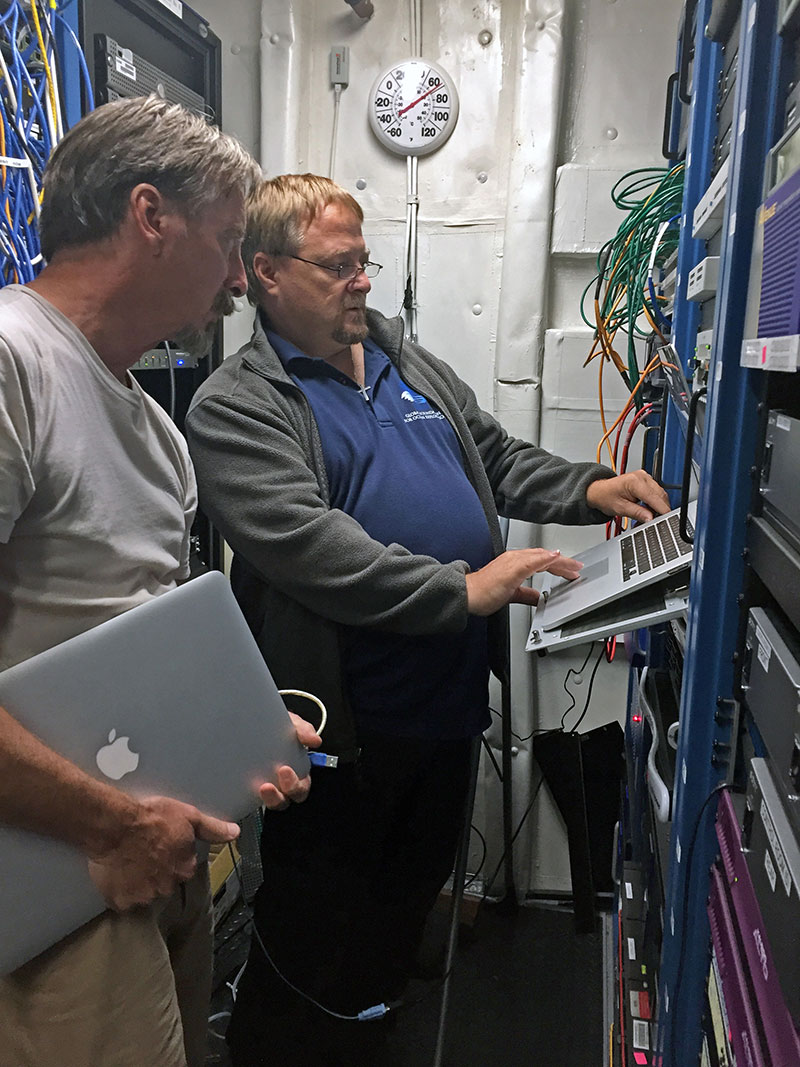 Telepresence Engineer, Roland Brian, and Senior Electrical Engineer, Dave Wright, verifying configuration of the telepresence network switch in the ship’s rack room. During shakedown operations, the ship-to-shore video streams need to be re-established.