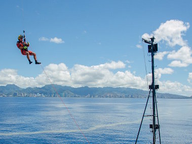 A U.S. Coast Guard rescue swimmer is deployed to the bow of NOAA Ship Okeanos Explorer during a training drill off the coast of Oahu, Hawaii.