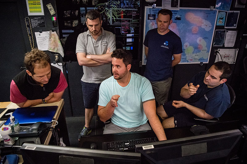 Lead Scientists, Daniel Wagner and Adam Skarke (from the left), discuss mapping with NOAA Ship Okeanos Explorer Mapping Lead, Mike White (center), Global Foundation for Ocean Exploration ROV Team Lead Karl McKletchie (second from right), and Expedition Coordinator, LT Nick Pawlenko (far right).