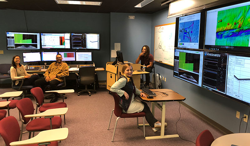 Image of NOAA Ship Okeanos Explorer onshore mapping team at the University of New Hampshire Exploration Command Center participating through telepresence. This image includes three of the Explorers in Training that participated in this expedition from shore.