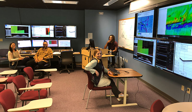 Image of NOAA Ship <em>Okeanos Explorer</em> onshore mapping team at the University of New Hampshire Exploration Command Center participating through telepresence. This image includes three of the Explorers-in-Training who participated in this expedition from shore.