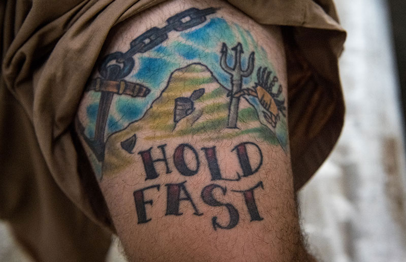 The words “Hold Fast” tattooed on Pete’s leg are a common nautical term signifying ‘not letting go’. It is traditionally written across a seaman’s knuckles.  The trident featured alongside represents King Neptune and was earned during Pete’s equator crossing ceremony; the crab and tin can are simply for artistic expression: “I was just having some fun with it” Pete says.