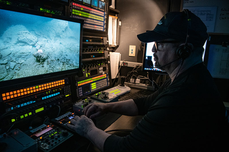 Video Engineer Brian Doros controlling video shading during a ROV dive of the Deep Connections 2019 expedition. Video shading refers to the task of controlling the ROV cameras to ensure that images are well lit and in focus. Image courtesy of NOAA Ocean Exploration, Deep Connections 2019.
