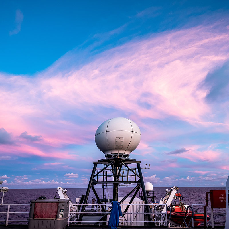 The sun sets over the VSAT or Very Small Aperture Terminal antenna that allows for real-time sharing of our exploration data and live video through telepresence. Image courtesy of Art Howard, Global Foundation for Ocean Exploration, Windows to the Deep 2019.