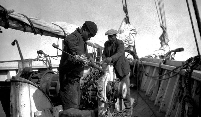 In this photo aboard a whaling ship in the Pacific, a boat steerer and foremast hand are fastening a harpoon to its pole.