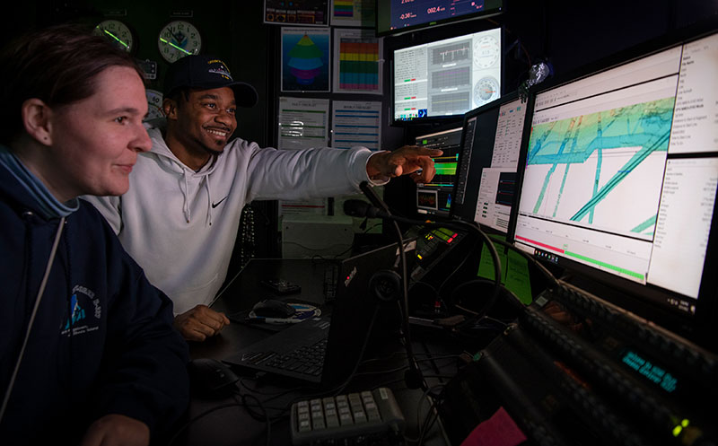 Explorers-in-Training Daryin Medley and Kathrin Bayer in the control room of NOAA Ship Okeanos Explorer viewing multibeam bathymetry data collected during the 2022 Caribbean Mapping expedition. Image courtesy of Caitlin Bailey, GFOE, 2022 Caribbean Mapping.