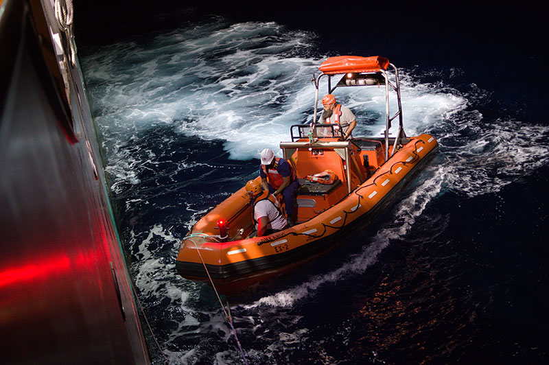 Members of the NOAA Ship Okeanos Explorer crew approach the ship after conducting small boat operations at night during the 2022 Caribbean Mapping expedition.